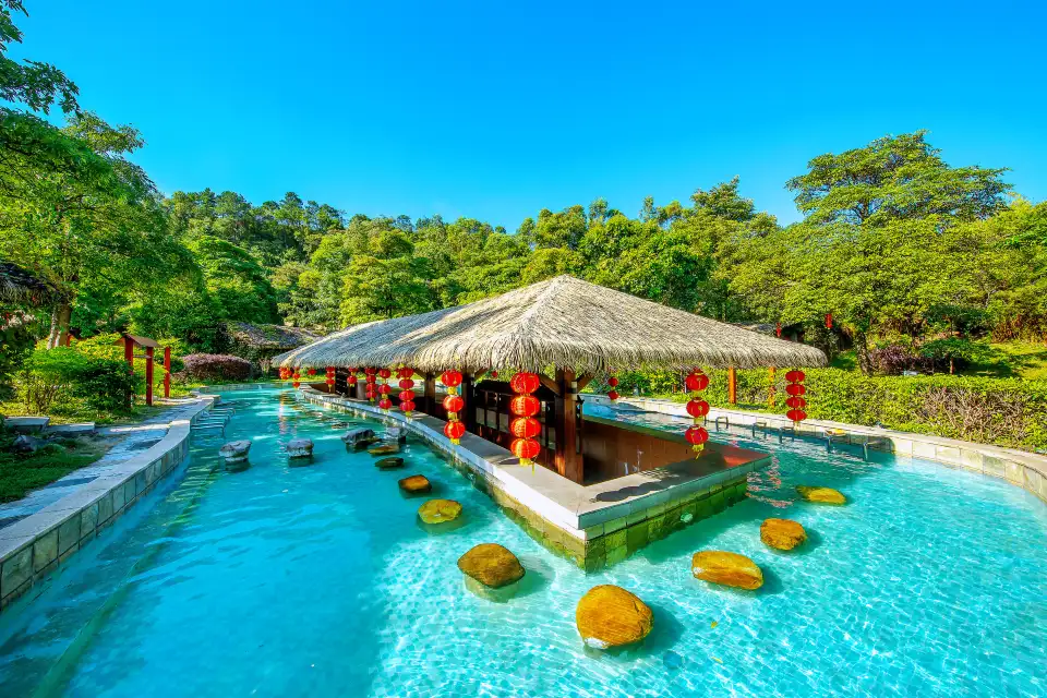 Turquoise hot spring pools winding past a thatched-roof pavilion strung with red lanterns