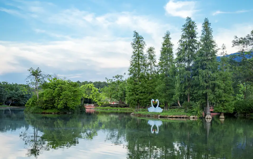 Still lake with swan sculpture and tall forest trees