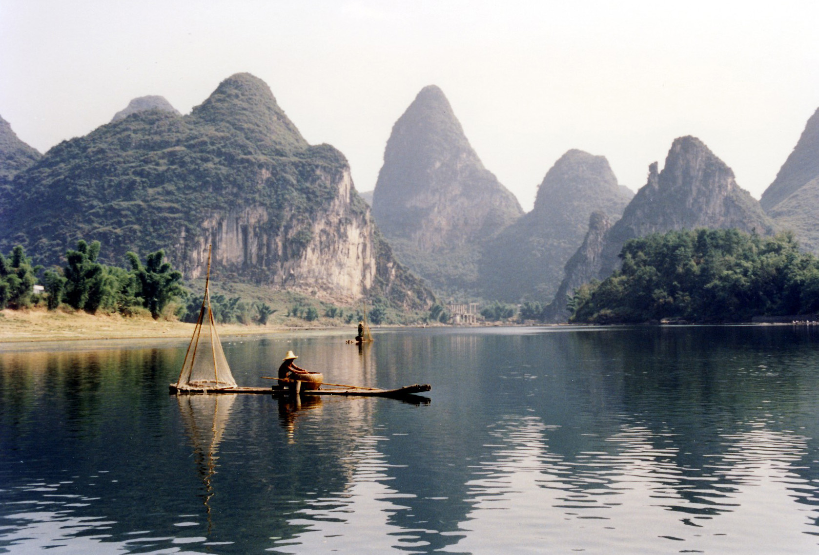 A fisherman on a bamboo raft with karst peaks reflected in still water